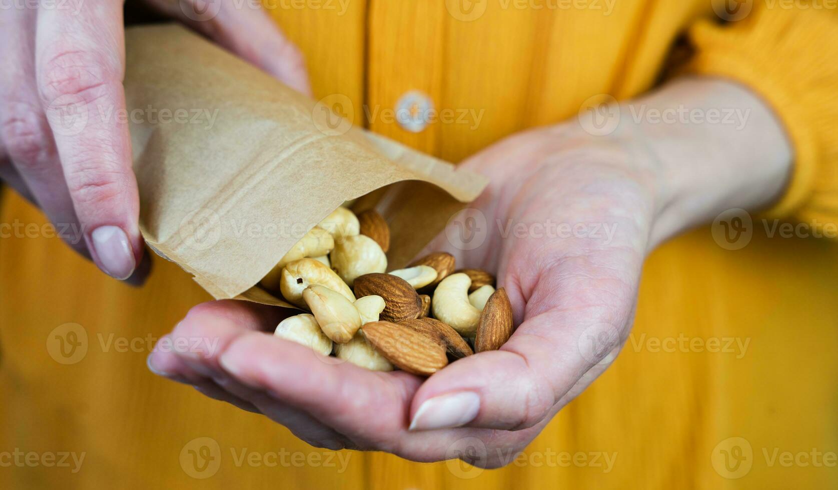 das Mädchen gießt ein mischen von Nüsse von ein Papier Tasche in ihr Hand. gesund Frühstück. gesund Essen Konzept. Nahansicht. selektiv Fokus. foto