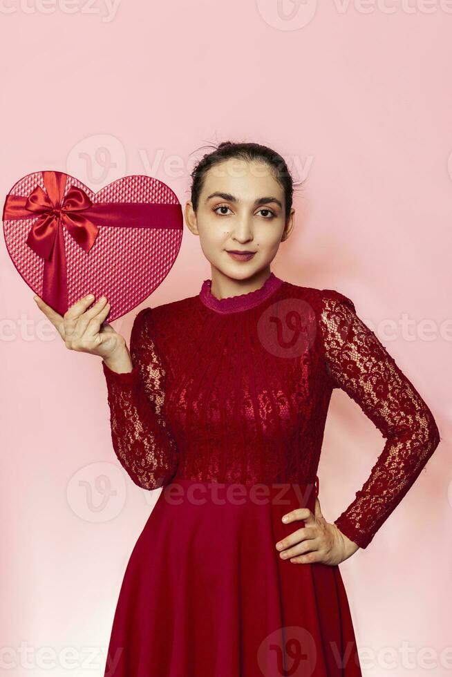 Porträt von attraktiv spanisch Frau halten Geschenkbox. Valentinsgrüße Tag Geschenke. schön Naher Osten Mädchen erhält herzförmig Geschenk Kasten. Liebe Tag, Jubiläum, Geburtstag Feier foto