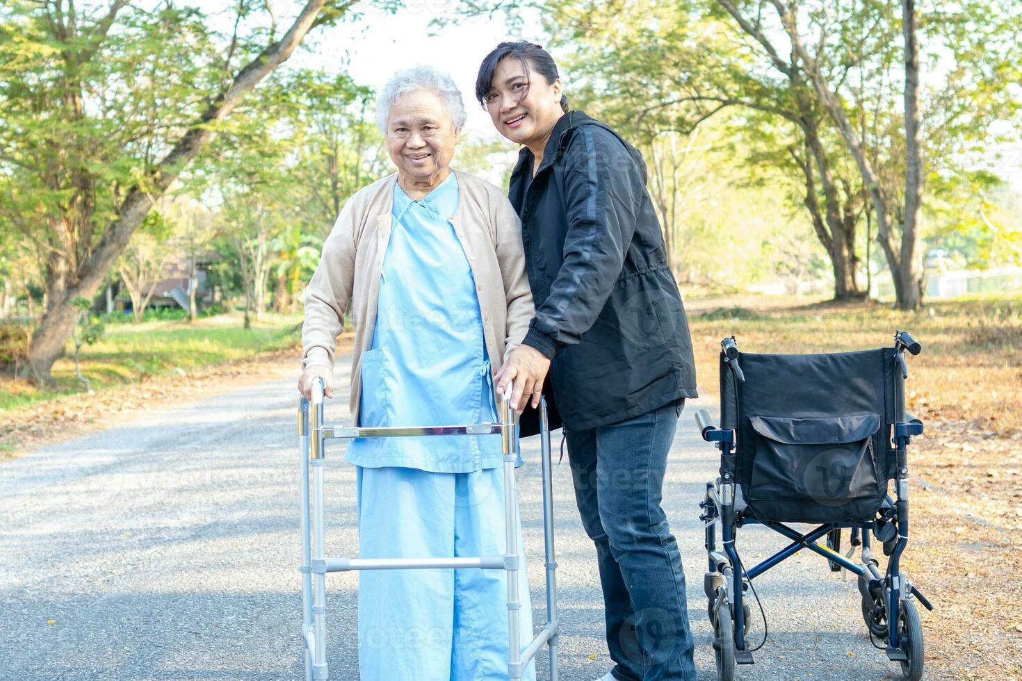 Pflegekraft Hilfe asiatisch Senior Frau gehen mit Gehhilfe mit Rollstuhl beim Park. foto