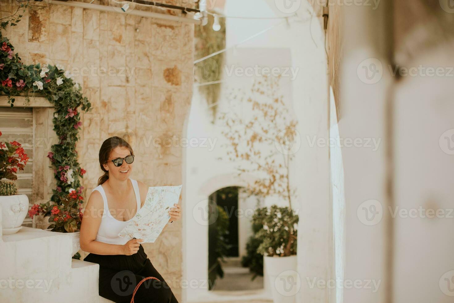 weiblich Tourist mit Papier Stadt Karte auf eng Straßen von Ostuni, Italien foto