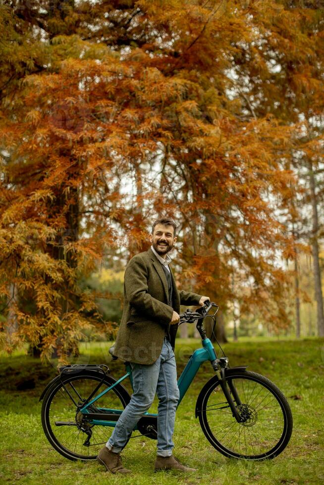 hübscher junger Mann mit Elektrofahrrad im Herbstpark foto