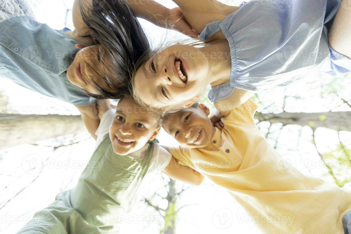 gruppe asiatischer und kaukasischer glücklicher kinder, die sich zusammenkauern, auf die kamera herabblicken und lächeln foto