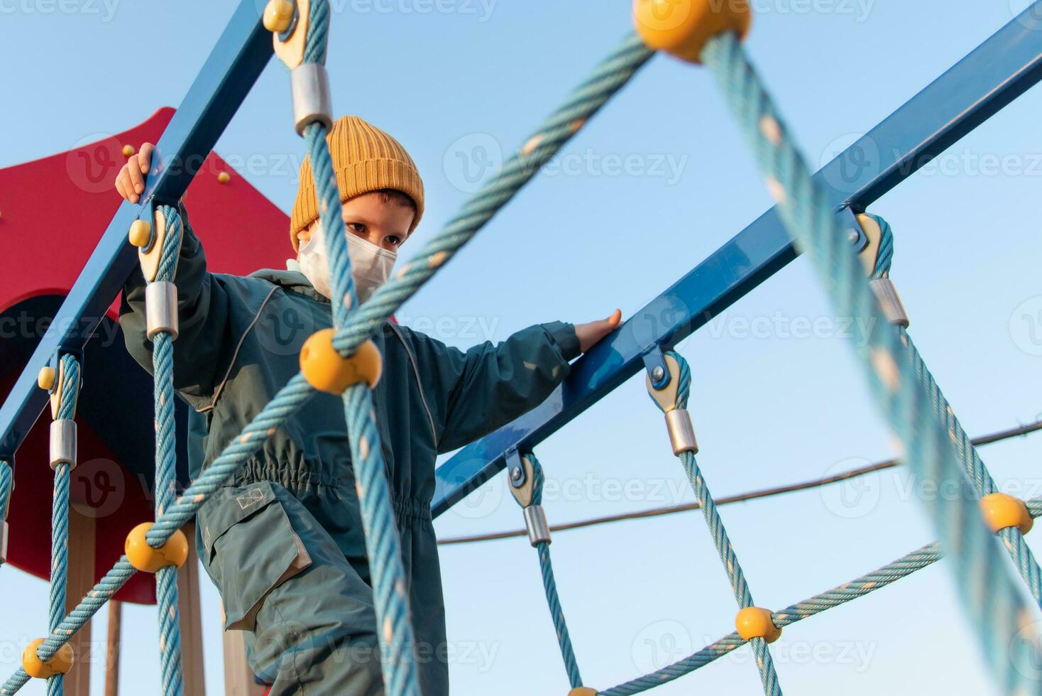 ein Kind im ein medizinisch Maske Theaterstücke auf das Spielplatz während das Pandemie von Coronavirus und covid - - 19 foto