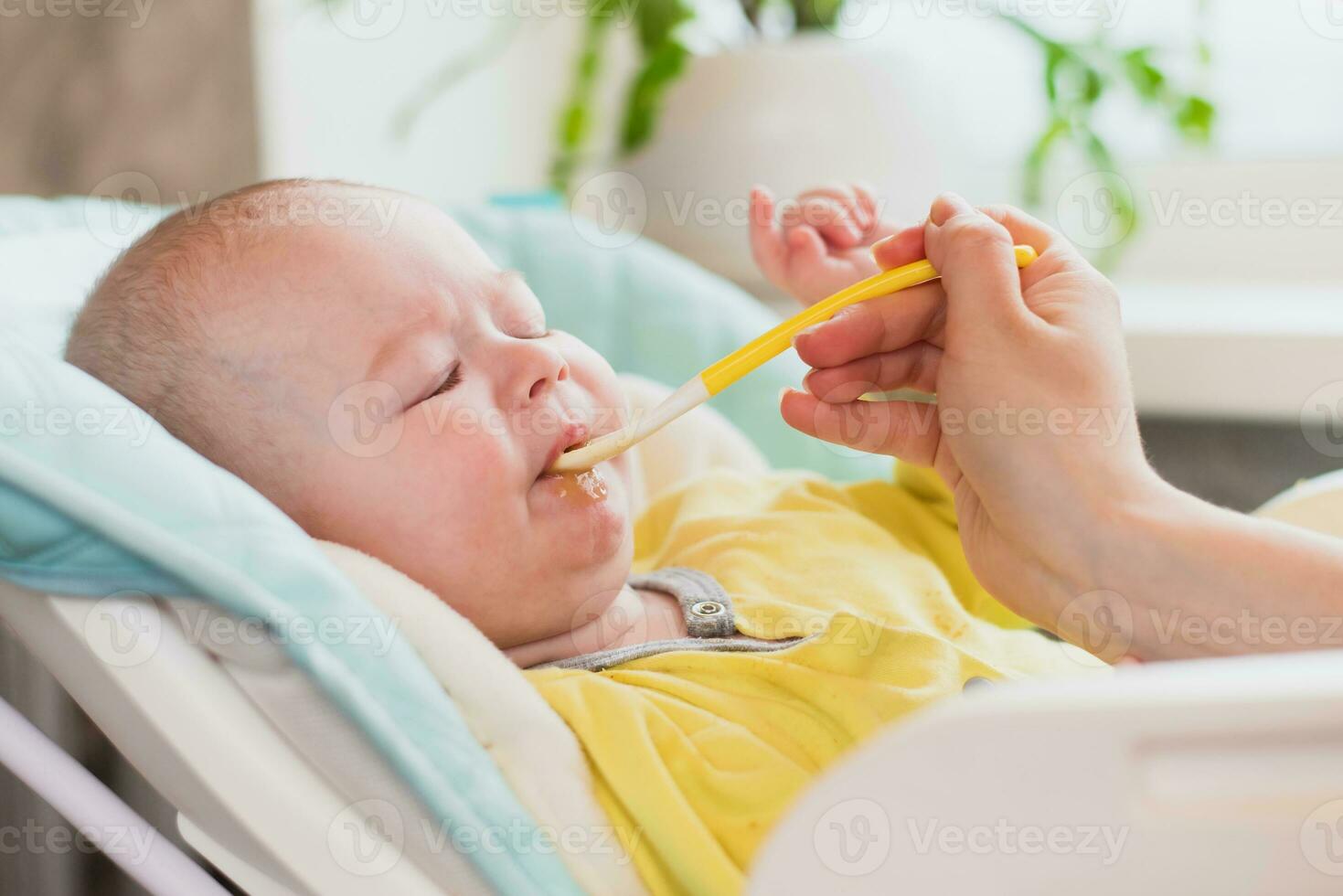 Mama Einspeisungen das Baby. das Mutter setzt ein Löffel von püriert im das Kinder Mund. das Kleinkind isst Lebensmittel. foto