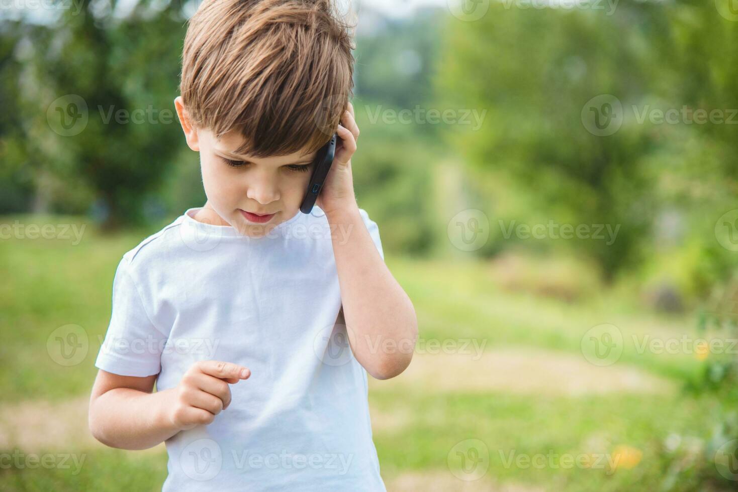 das Kind spricht auf das Telefon im Natur foto