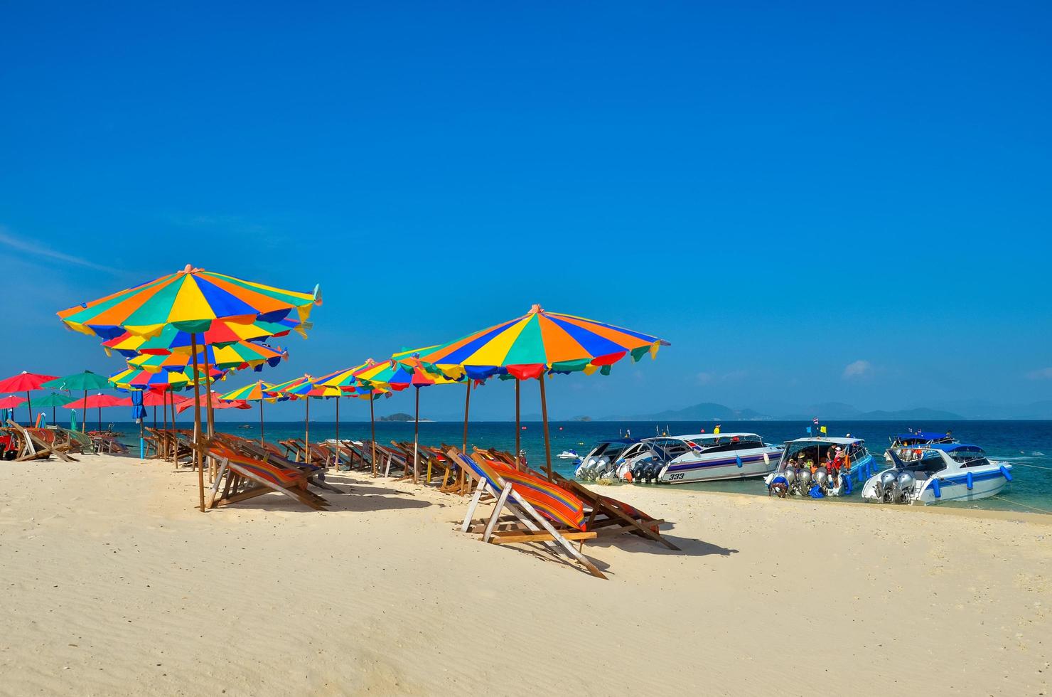 Phuket, Thailand, 2020 - Stühle und Sonnenschirme an einem Strand mit Menschen und Booten foto