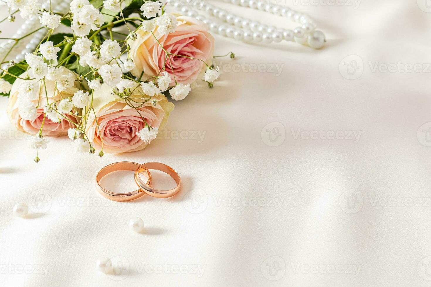 zart Hochzeit Anordnung mit zwei Hochzeit Gold Ringe auf ein Sahne Satin- Hintergrund mit Perle Perlen und Blumen. Postkarte. Einladung. Abdeckung. foto