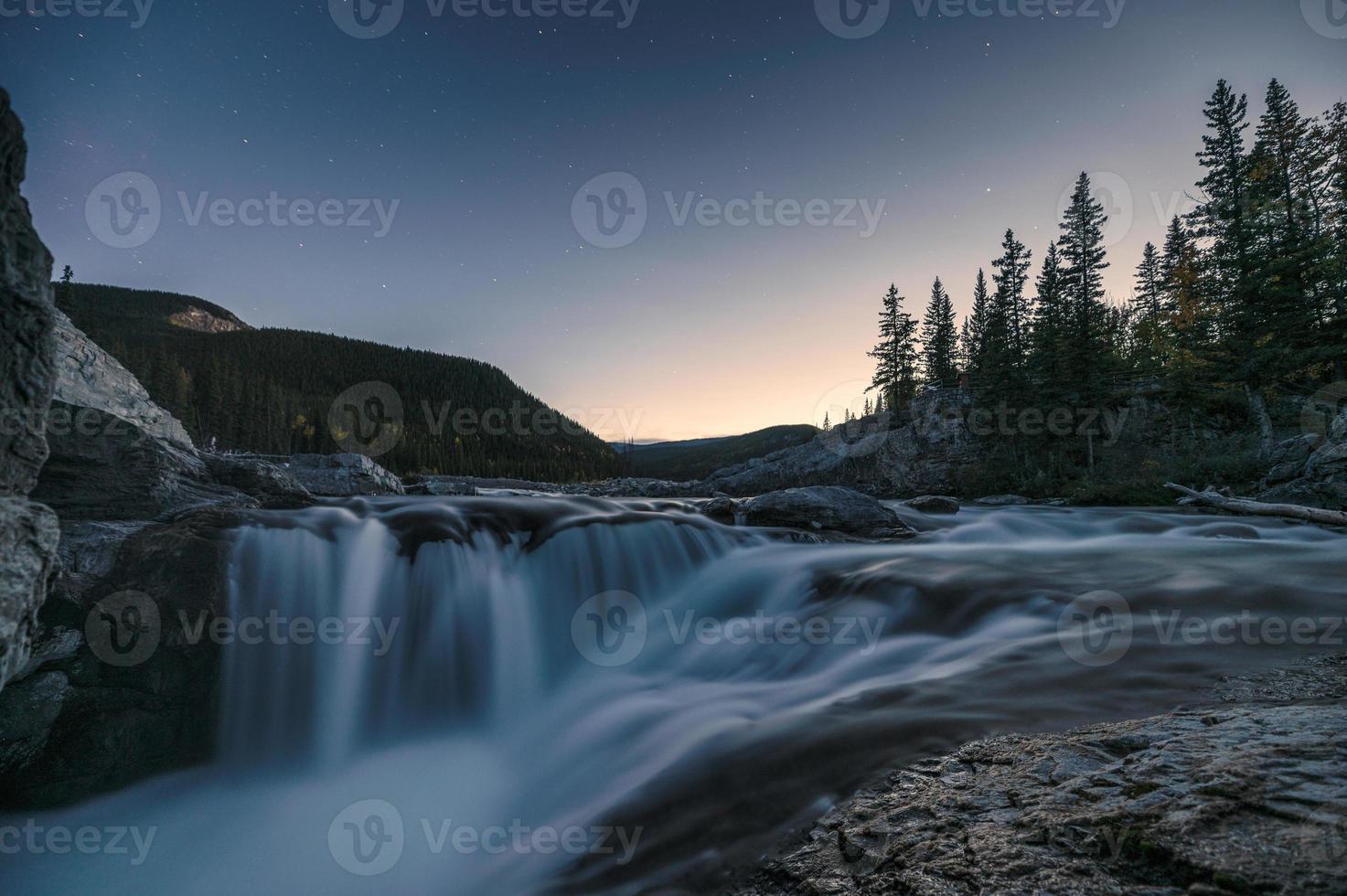 Wasserfall Stromschnellen, die am Abend bei Ellbogenfällen auf Felsen im Kiefernwald fließen foto