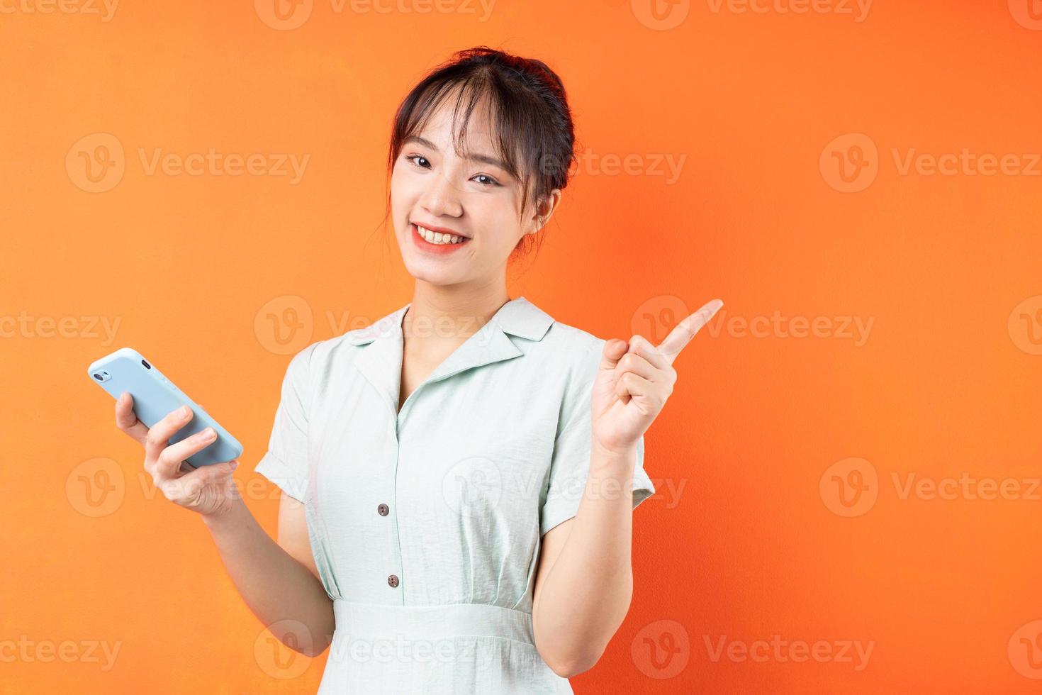 Porträt eines jungen Mädchens, das Telefon benutzt und nach rechts zeigt, isoliert auf orangem Hintergrund foto