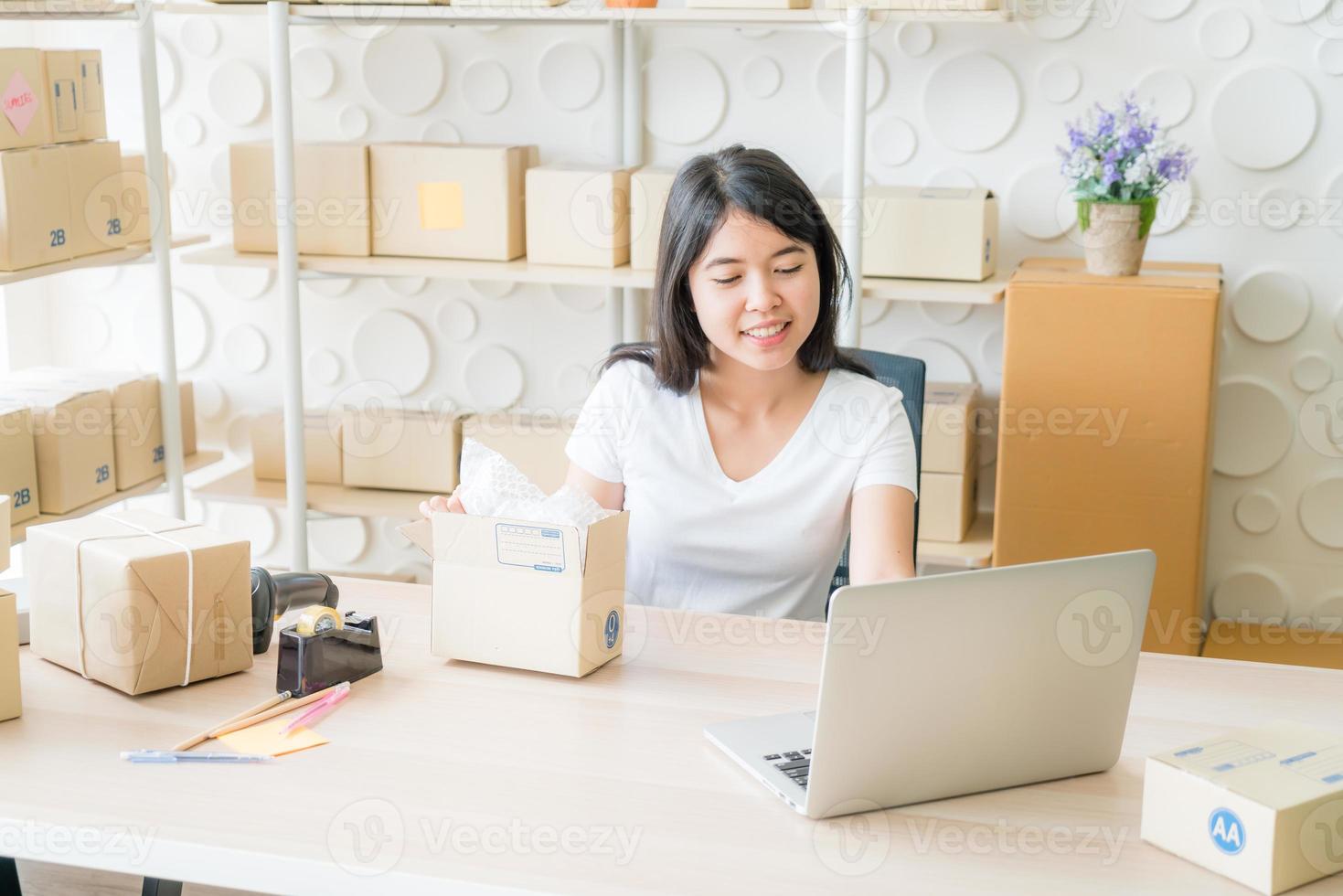 Asiatische Geschäftsinhaberin, die zu Hause mit Verpackungsbox am Arbeitsplatz arbeitet foto