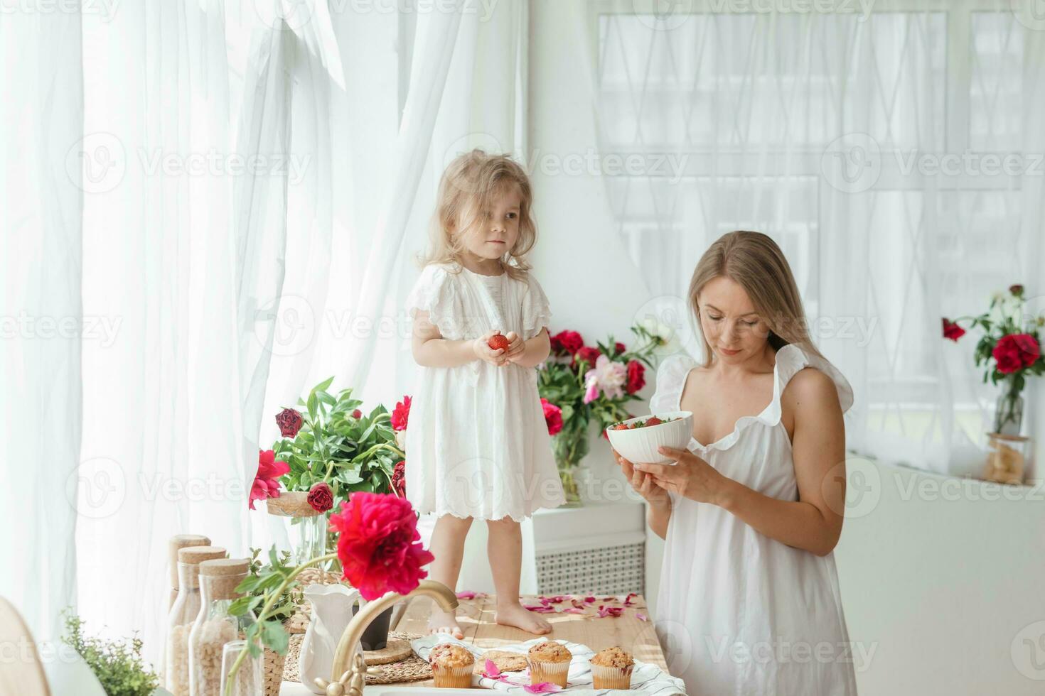 ein wenig blond Mädchen mit ihr Mama auf ein Küche Arbeitsplatte dekoriert mit Pfingstrosen. das Konzept von das Beziehung zwischen Mutter und Tochter. Frühling Atmosphäre. foto