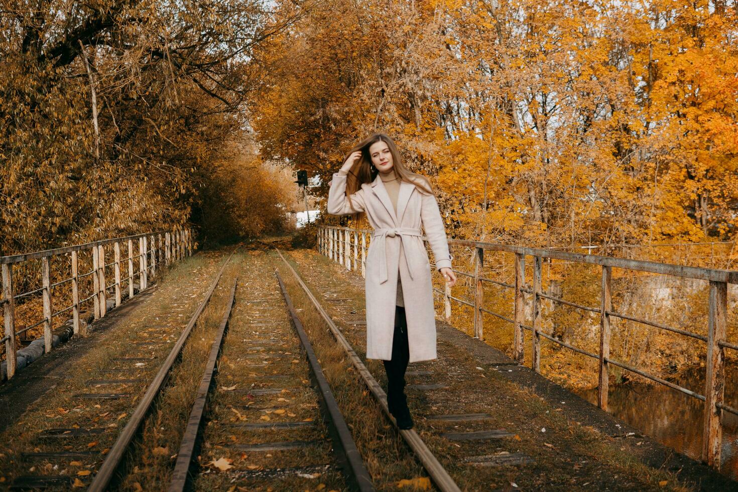 schön langhaarig Frau Spaziergänge durch das Herbst Straßen. Eisenbahn, Herbst, Frau im ein Mantel. foto