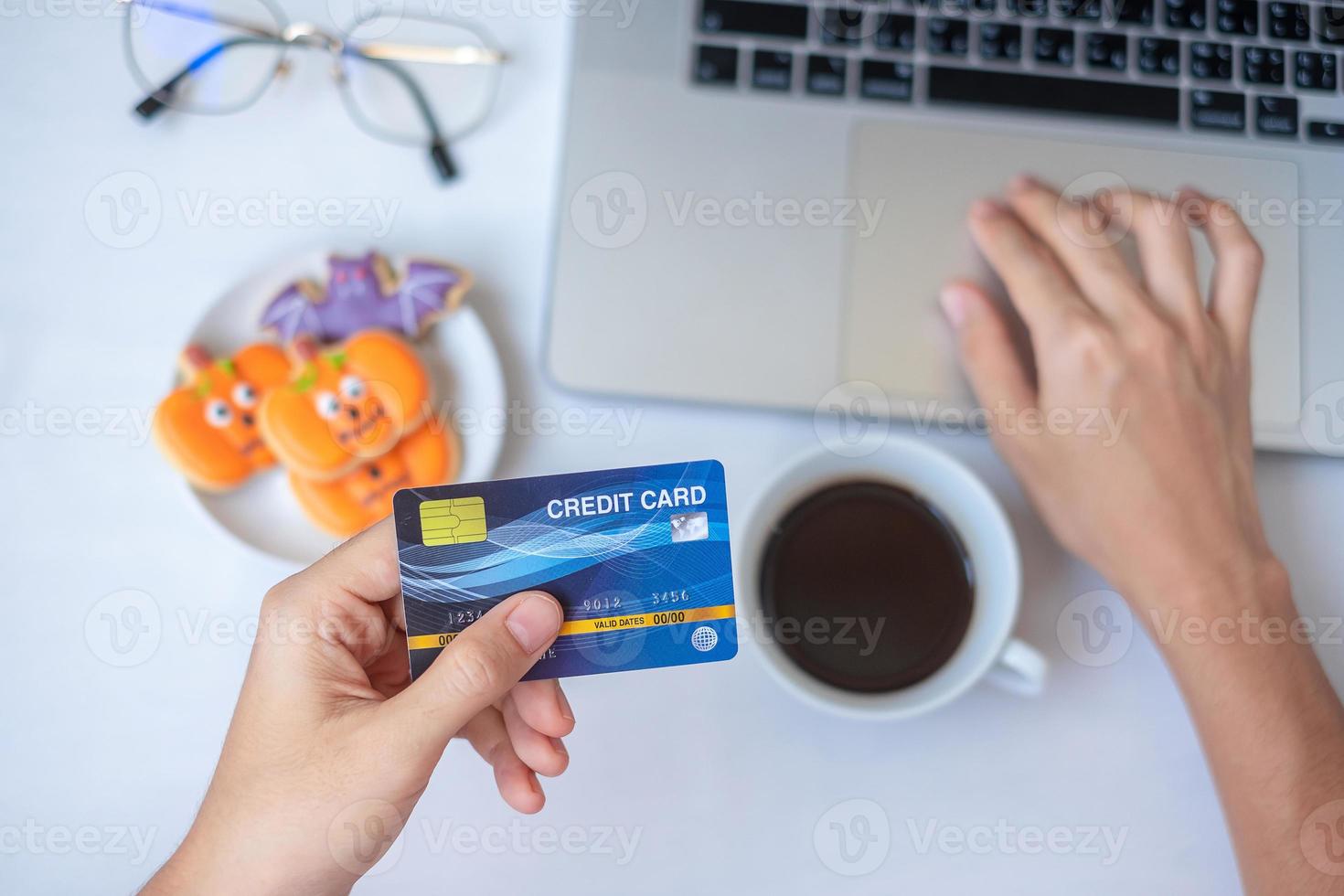 Hand mit Kreditkarte für Online-Shopping auf dem Laptop während des Essens von Halloween-Keksen und Kaffee. Happy halloween, hallo oktober, herbst, festlich, party und ferienkonzept foto