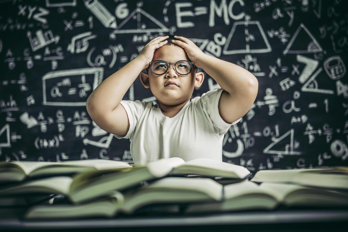 Jungen mit Brille schreiben Bücher und denken im Klassenzimmer nach foto