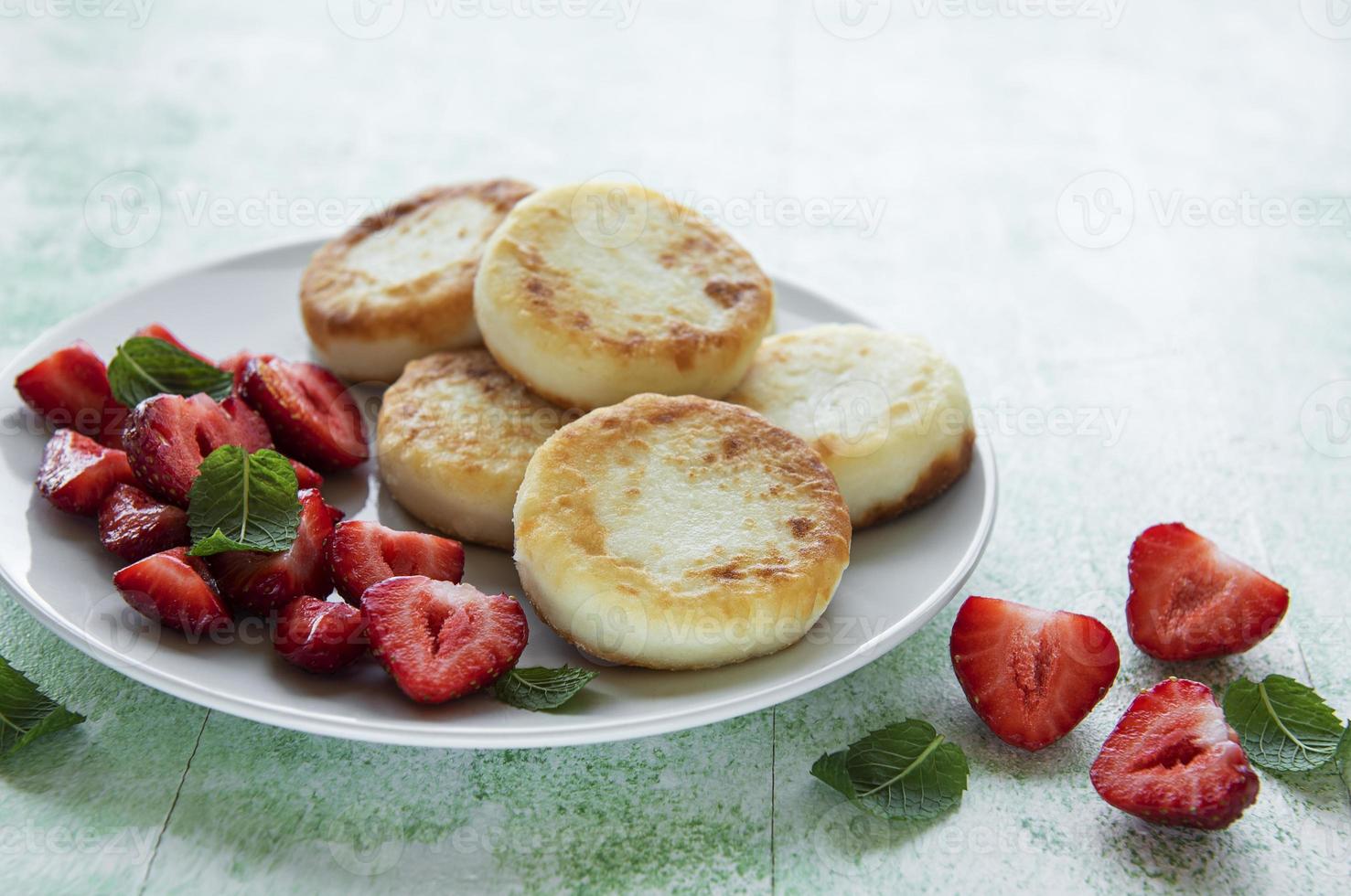 Quarkpfannkuchen, Ricotta-Krapfen auf Keramikplatte mit frischer Erdbeere. foto