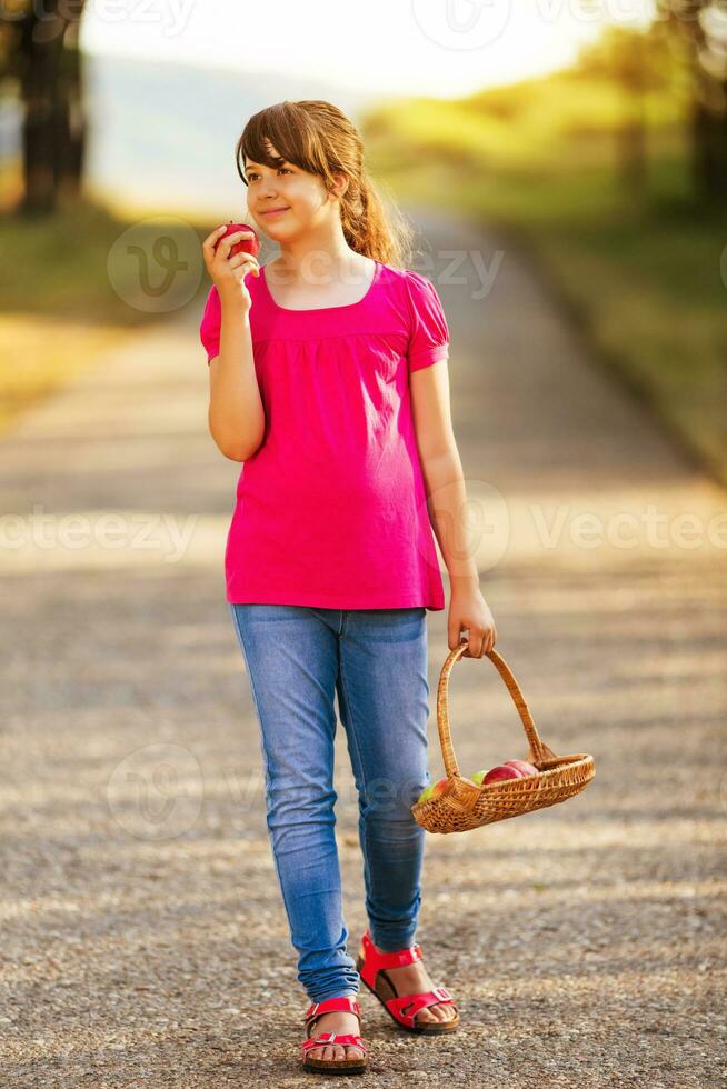 schön wenig Mädchen genießt Essen Apfel während Gehen im das Natur foto