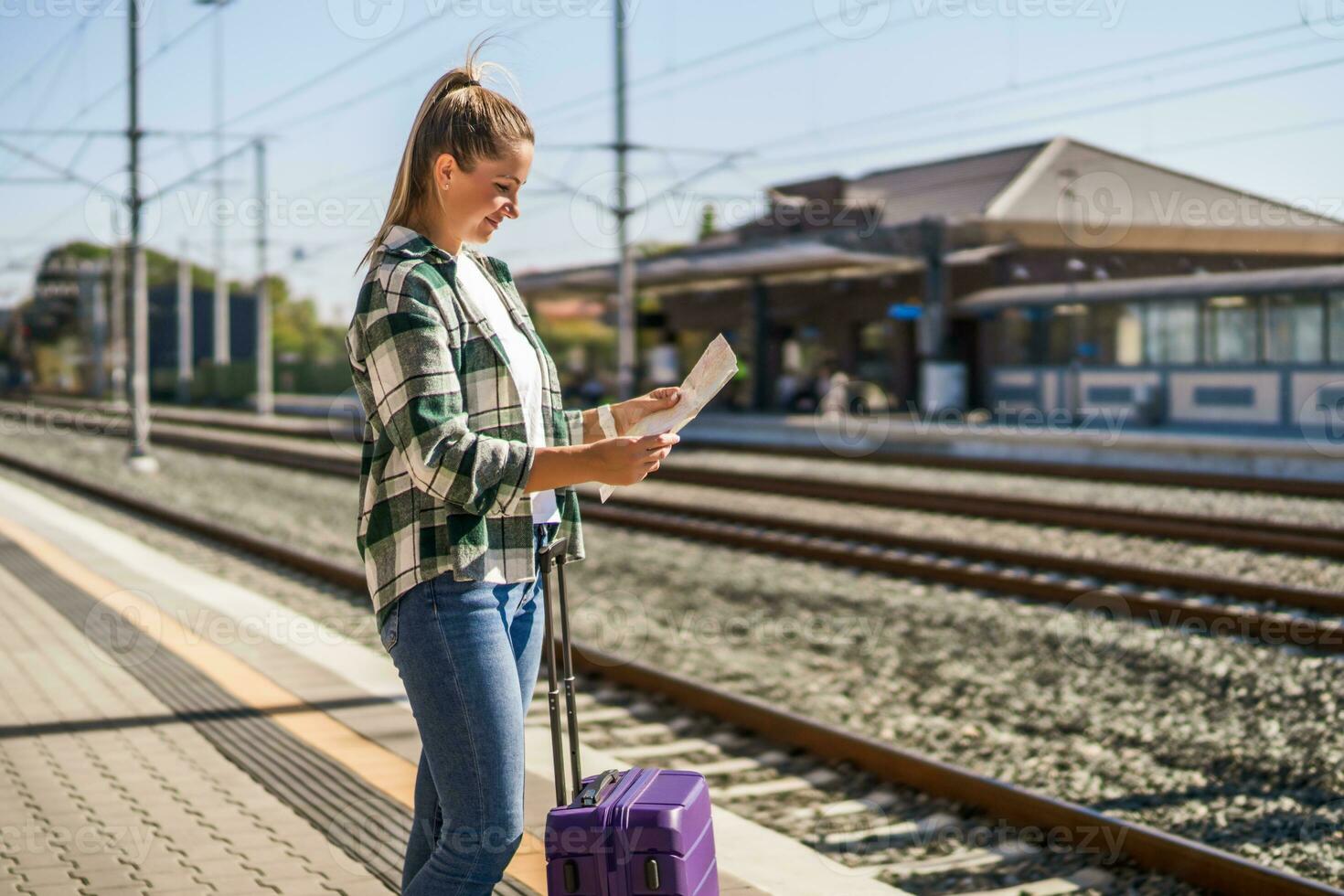 glücklich Frau suchen beim Karte während Stehen auf ein Zug Bahnhof foto
