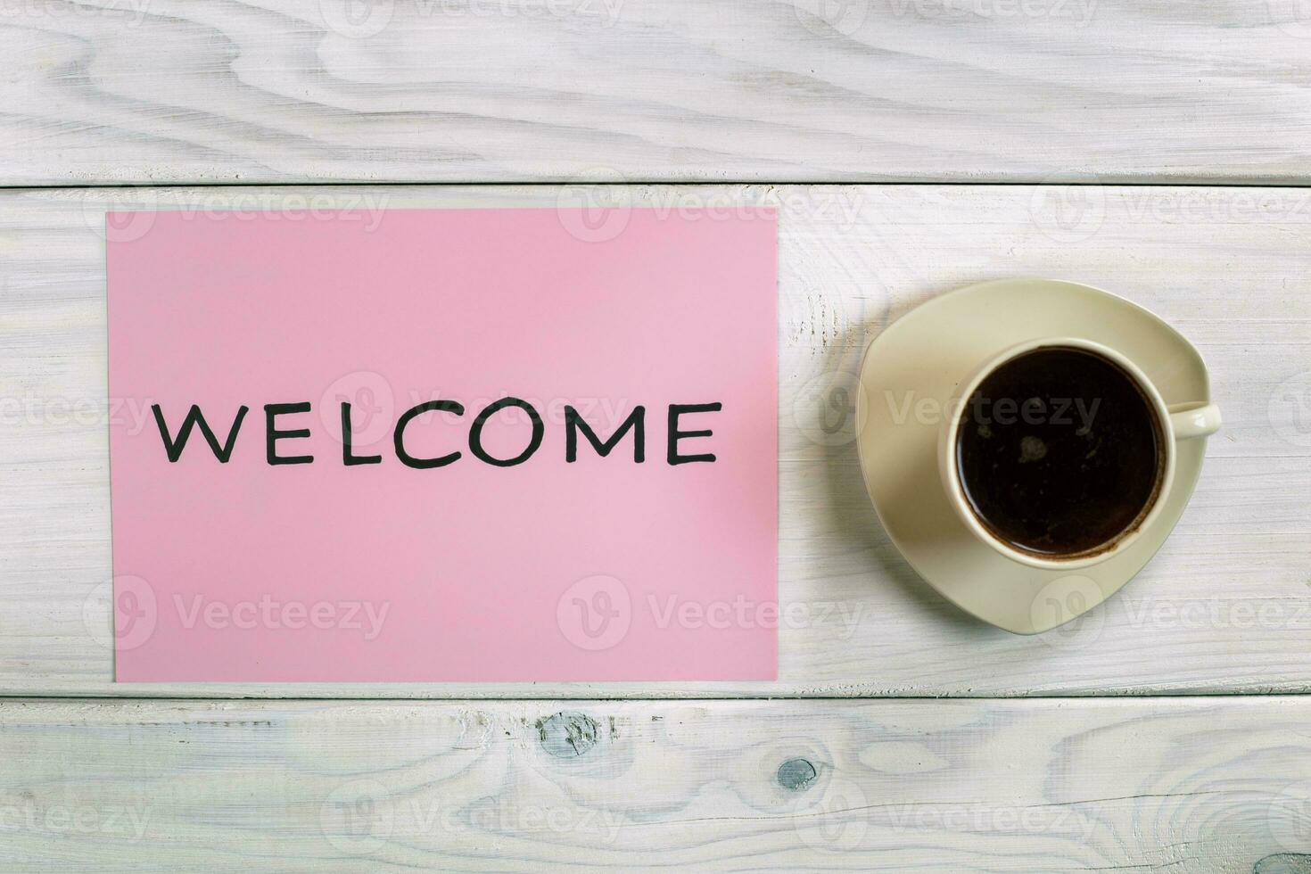 herzlich willkommen Zeichen auf Rosa Papier mit Tasse von Kaffee auf hölzern Tabelle foto