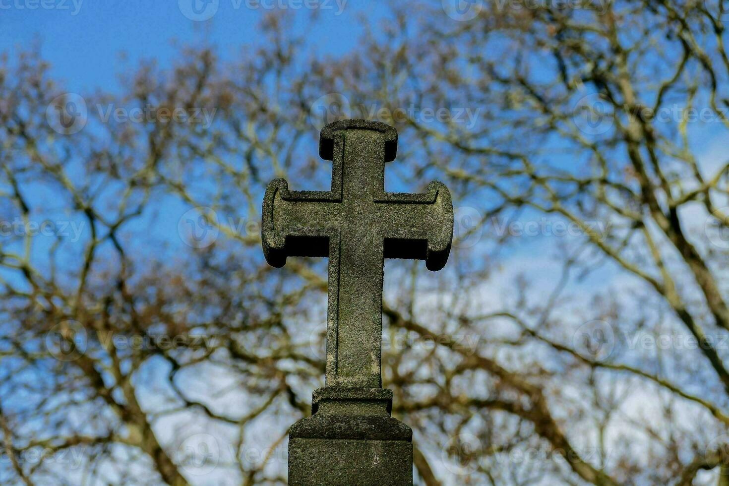 ein Kreuz auf oben von ein Grabstein im Vorderseite von Bäume foto