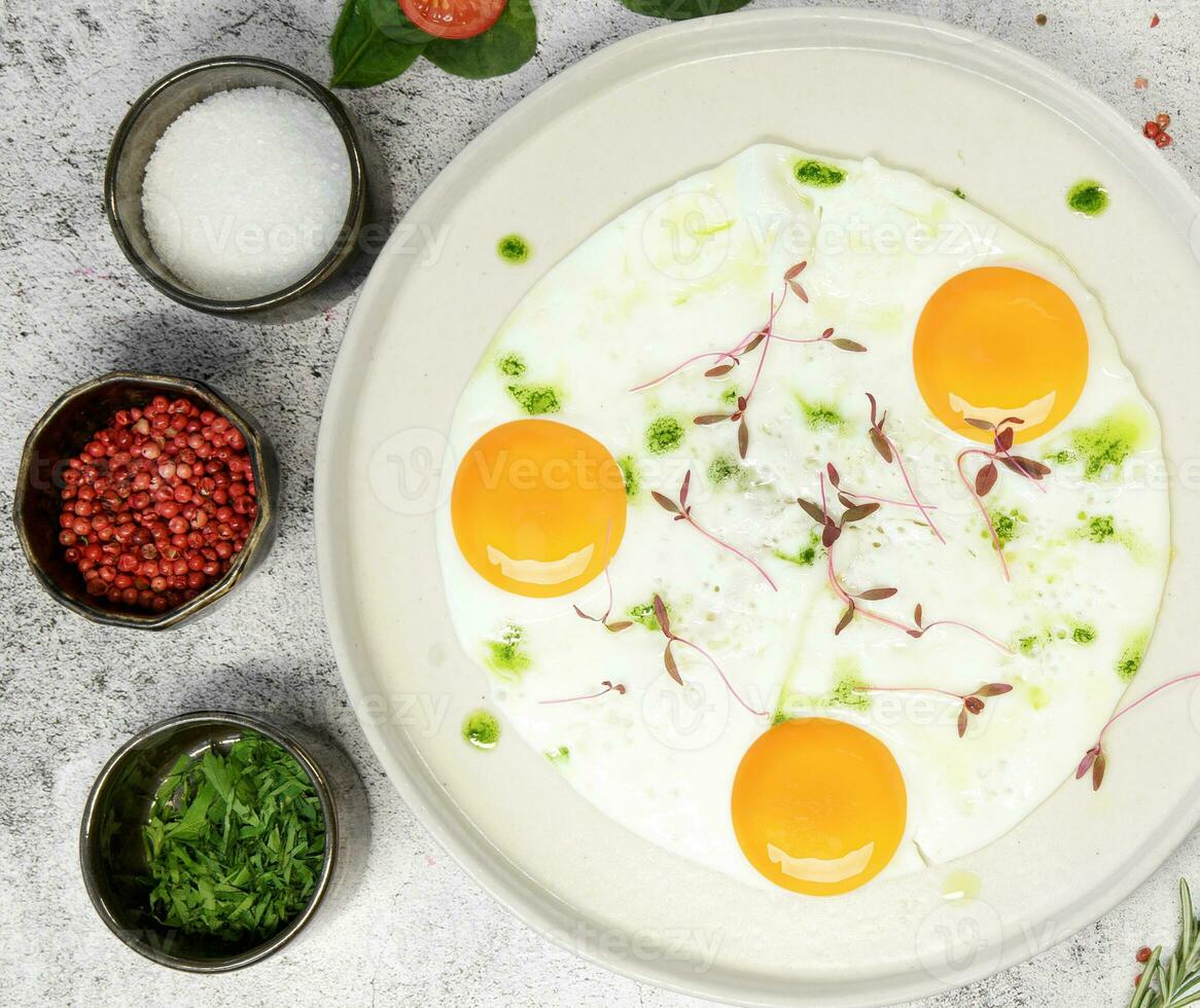 Frühstück. gebraten Eier von drei Eier sind bestreut mit Gras auf ein Licht Platte. Nächster zu Gewürze und Gewürze. hoch Qualität Foto