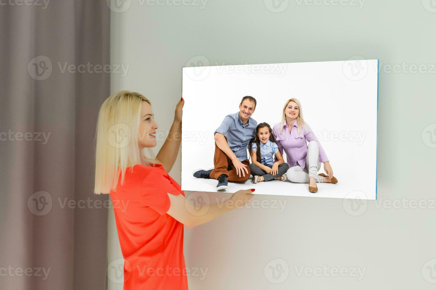 ein glücklich jung blond Frau ist halten ein groß Mauer Foto Segeltuch beim Zuhause