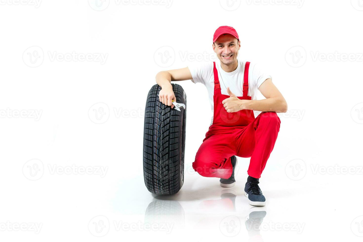 ein männlich Mechaniker posieren mit ein schonen Reifen und halten ein Schlüssel isoliert auf Weiß Hintergrund foto