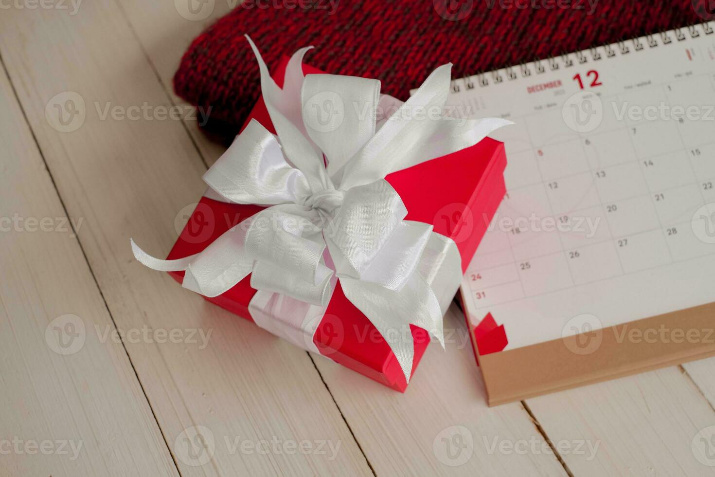 rot Geschenk Box und Kalender auf isoliert auf ein rot gestrickt Schal mit Weiß hölzern Hintergrund mit. Weihnachten Tag Konzept. Planung Planung Agenda, Fall, Veranstalter Weihnachten Tag. eben legen, oben Sicht. foto