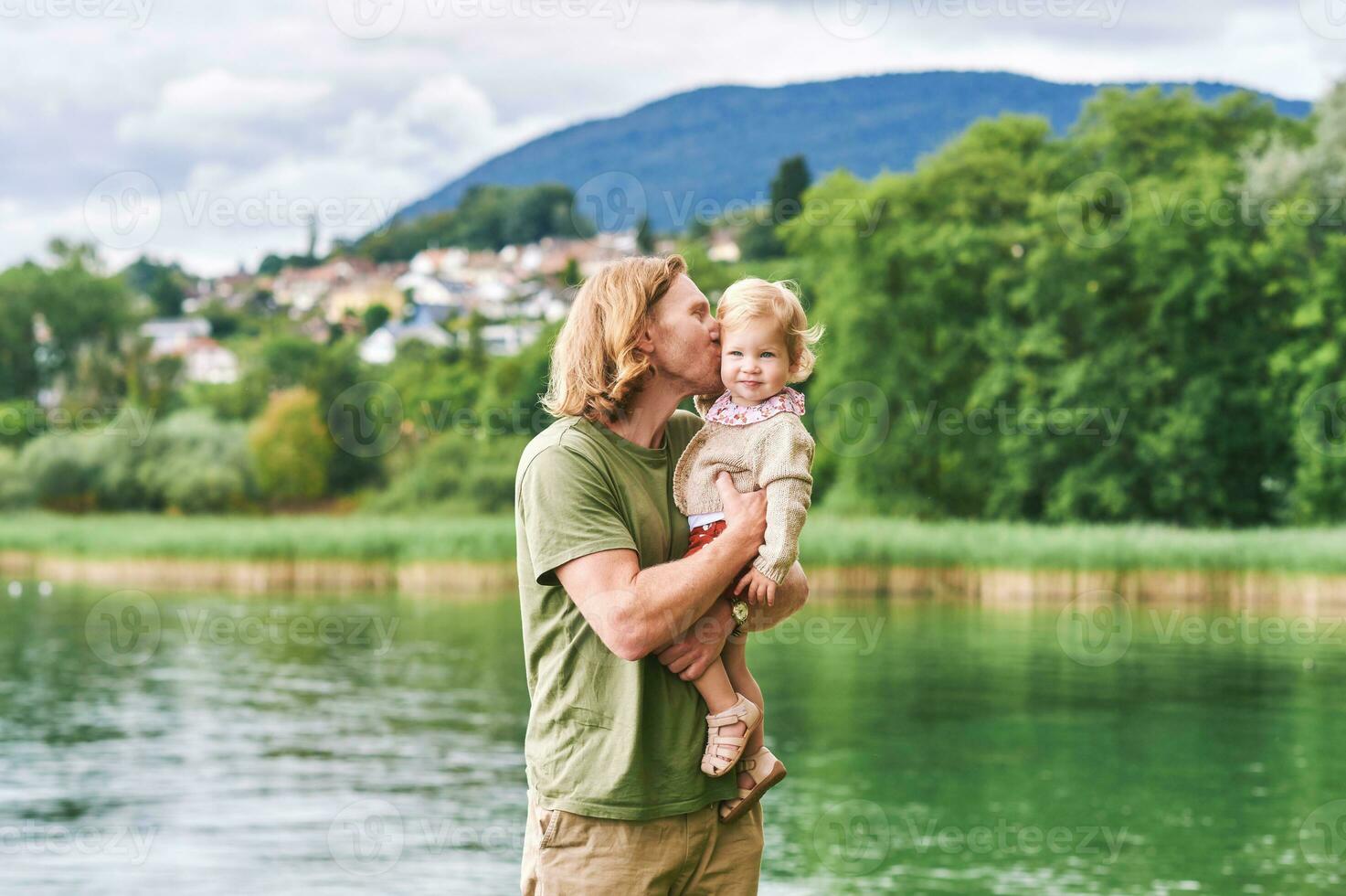 Porträt von glücklich jung Vater mit bezaubernd Kleinkind Mädchen spielen draußen Nächster zu See oder Fluss foto