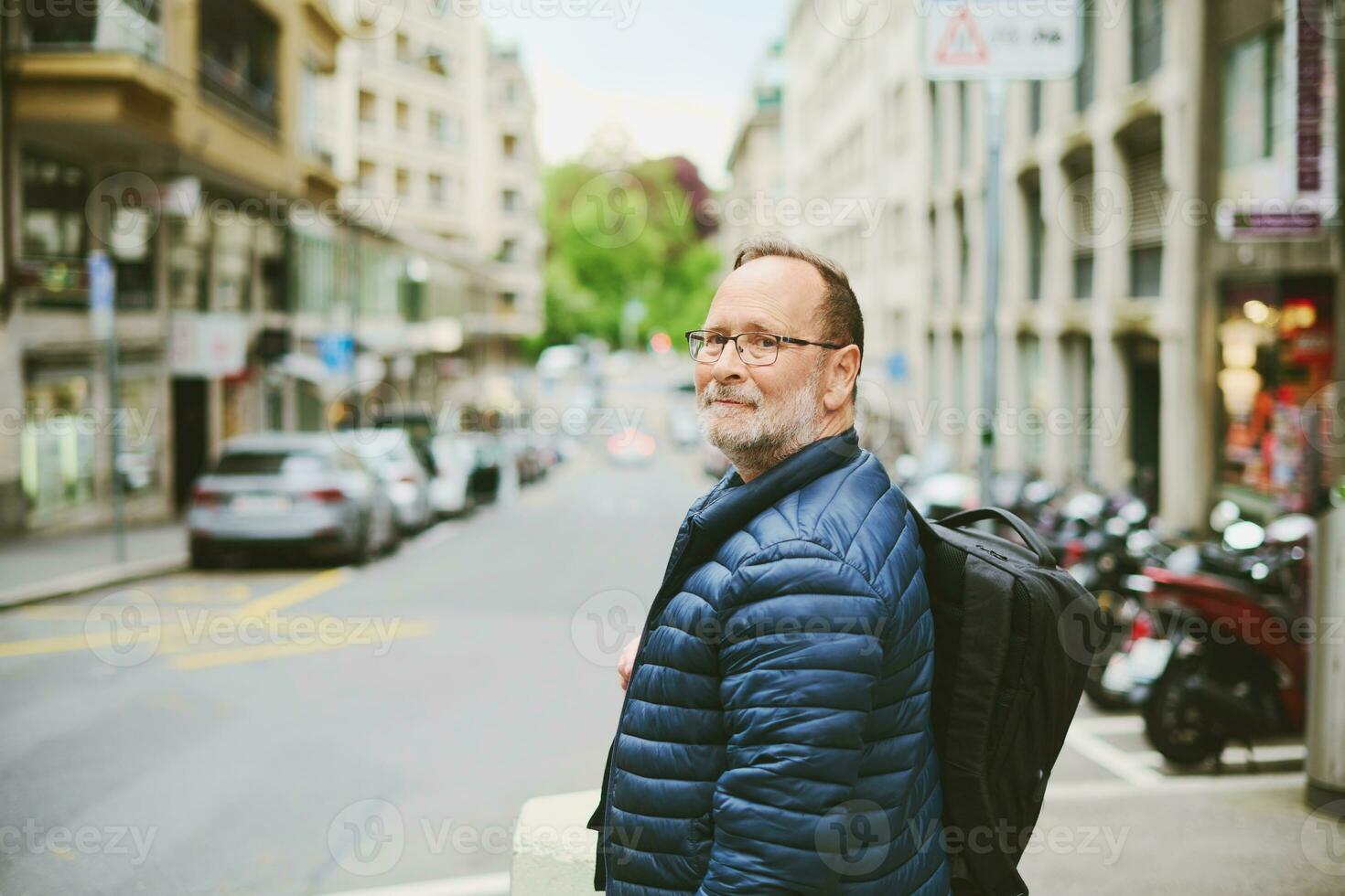 draussen Porträt von 55-60 Jahr alt Mann tragen Blau Jacke und Rucksack, suchen zurück Über das Schulter foto