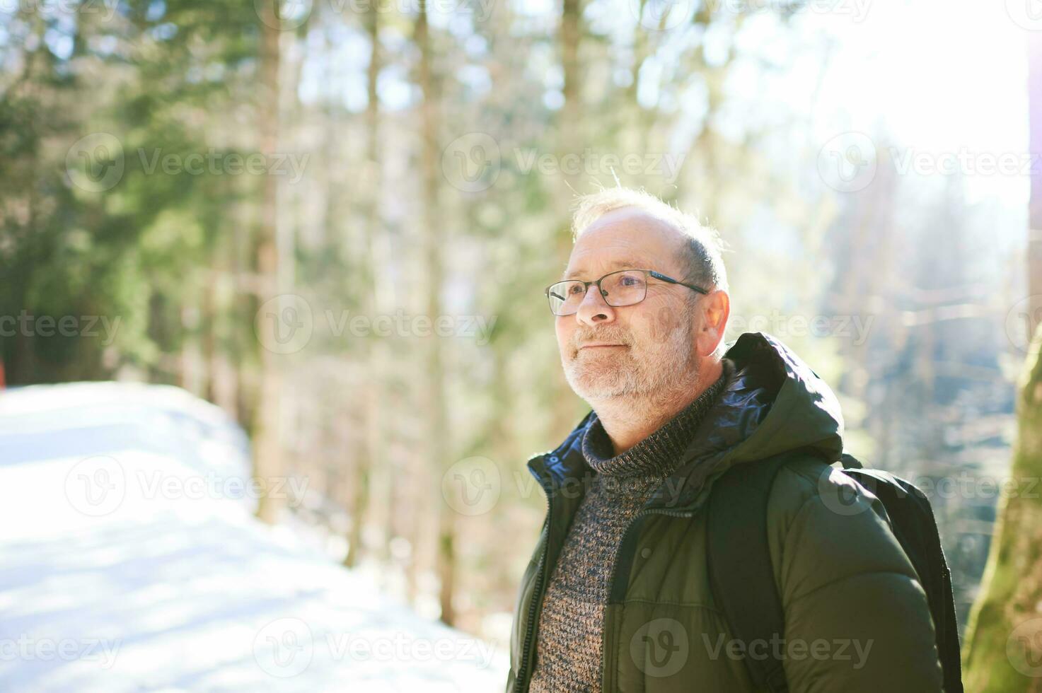 draussen Porträt von Mitte Alter 55 - - 60 Jahr alt Mann Wandern im Winter Wald, tragen warm Jacke und schwarz Rucksack foto