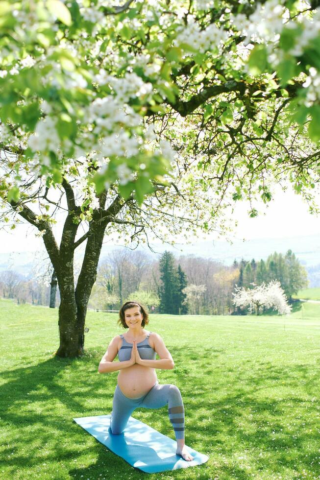 draussen Porträt von glücklich jung schwanger Frau üben duga im Frühling Garten unter Blühen Apfel Bäume, gesund Lebensstil foto
