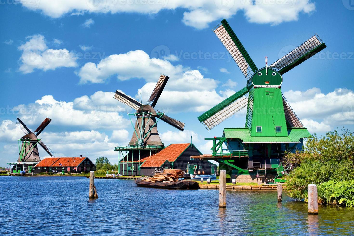 Niederländische Windmühle in grüner Landschaft in der Nähe von Amsterdam, Niederlande, mit blauem Himmel und Flusswasser. foto