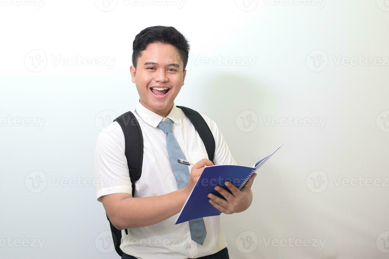 indonesisch Senior hoch Schule Schüler tragen Weiß Hemd Uniform mit grau Krawatte Schreiben auf Hinweis Buch mit Stift. isoliert Bild auf Weiß Hintergrund foto