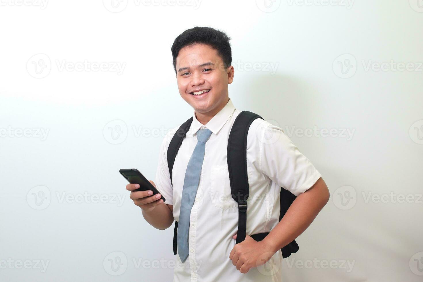 indonesisch Senior hoch Schule Schüler tragen Weiß Hemd Uniform mit grau Krawatte zeigen schockiert Gesicht Ausdruck während halten ein Handy, Mobiltelefon Telefon. isoliert Bild auf Weiß Hintergrund foto