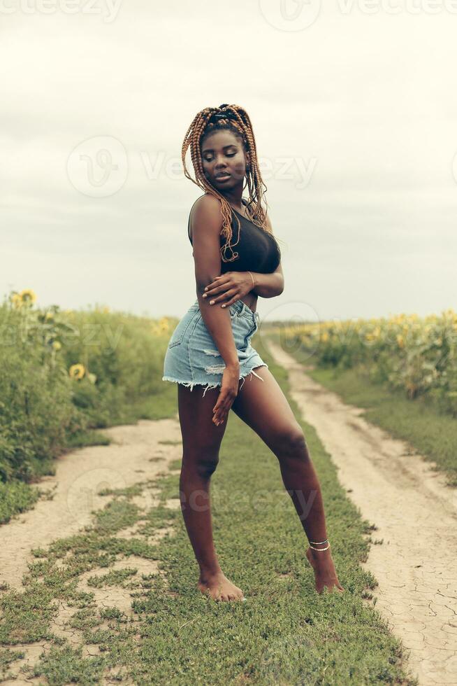 afrikanisch amerikanisch Mädchen im ein Feld von Gelb Blumen beim Sonnenuntergang foto