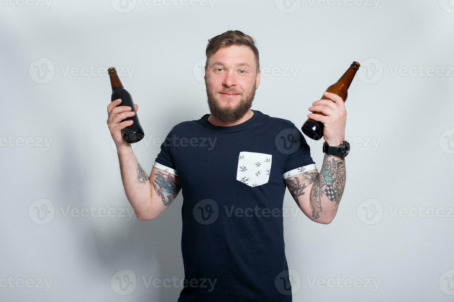 brutal bärtig männlich mit tätowiert Arm Getränke ein Bier von ein Flasche. foto