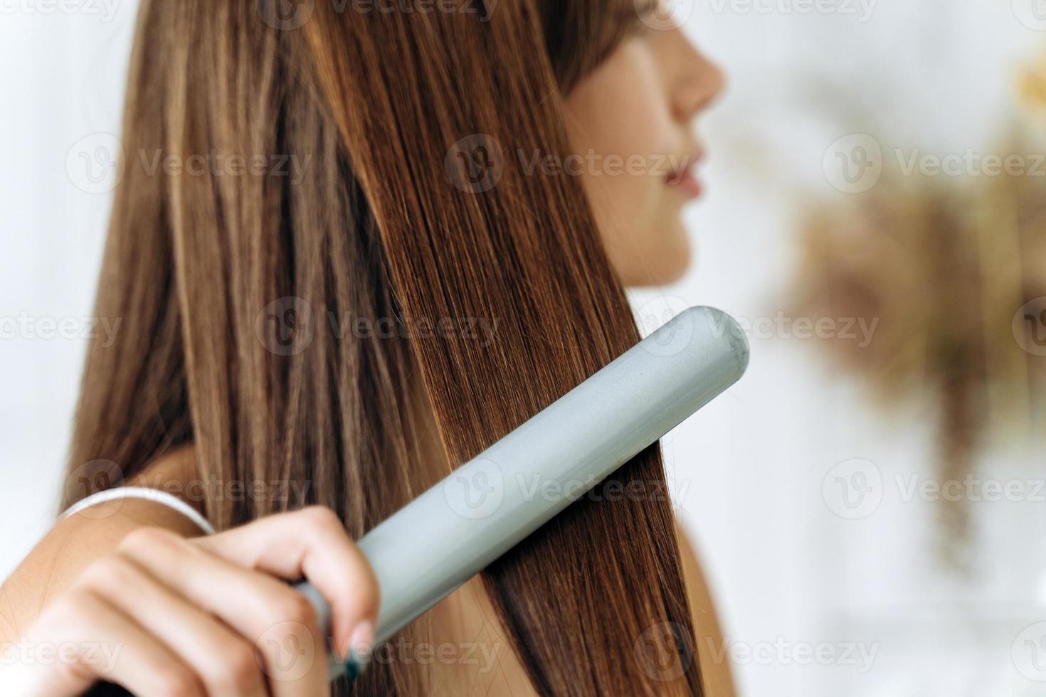 Friseur. Frau mit schönen langen glatten Haaren mit Haarglätter. wunderschönes Mädchen, das gesundes Haar mit Glätteisen glättet. Haarbügel- und Frisurenkonzept foto