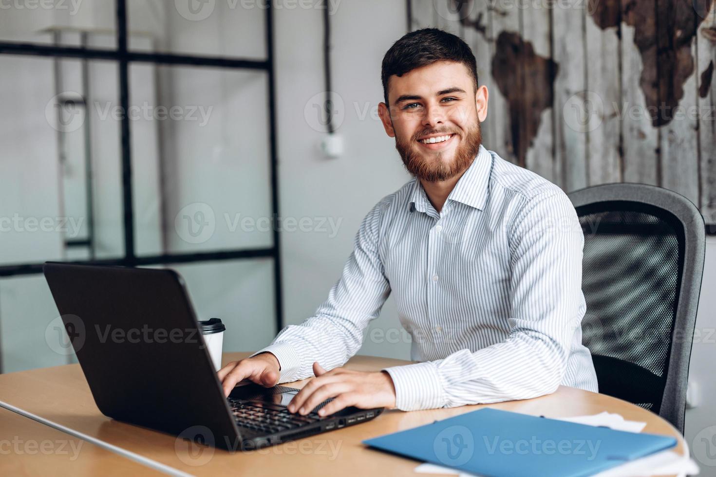 Lächelnder, bärtiger Mann, der im Büro am Computer arbeitet foto