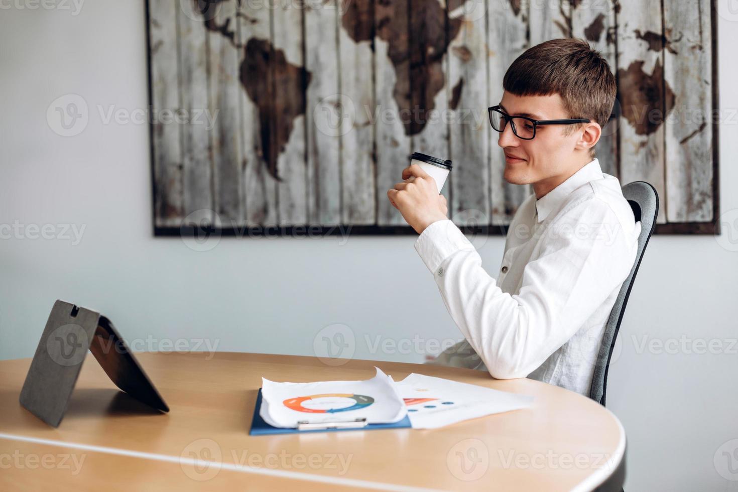 Junger Geschäftsmann mit Brille, der Kaffee trinkt und Nachrichten auf dem Tablet sieht foto