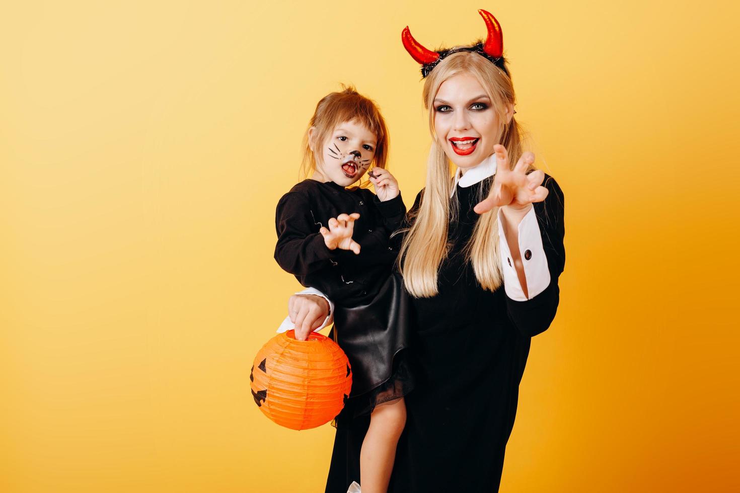 glückliche Emotion der Teufelsfrau, die vor einem gelben Hintergrund steht und ein kleines Mädchen hält foto