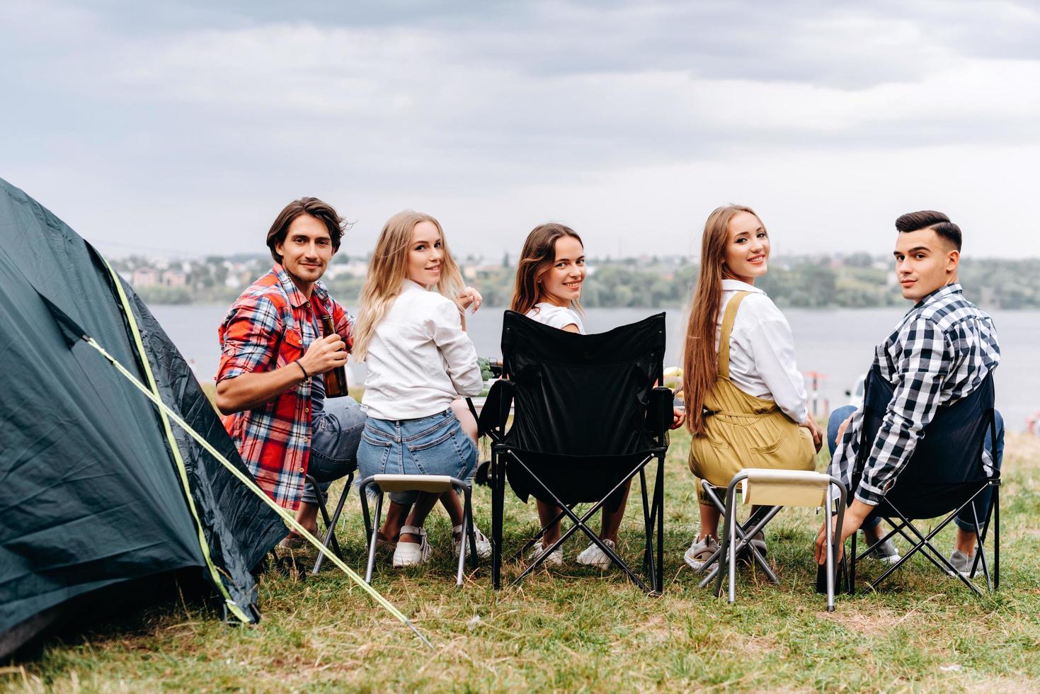 eine Gesellschaft von Freunden hat eine lustige Zeit auf dem Campingplatz. sie sitzen eine halbe Umdrehung. - Rückansicht foto