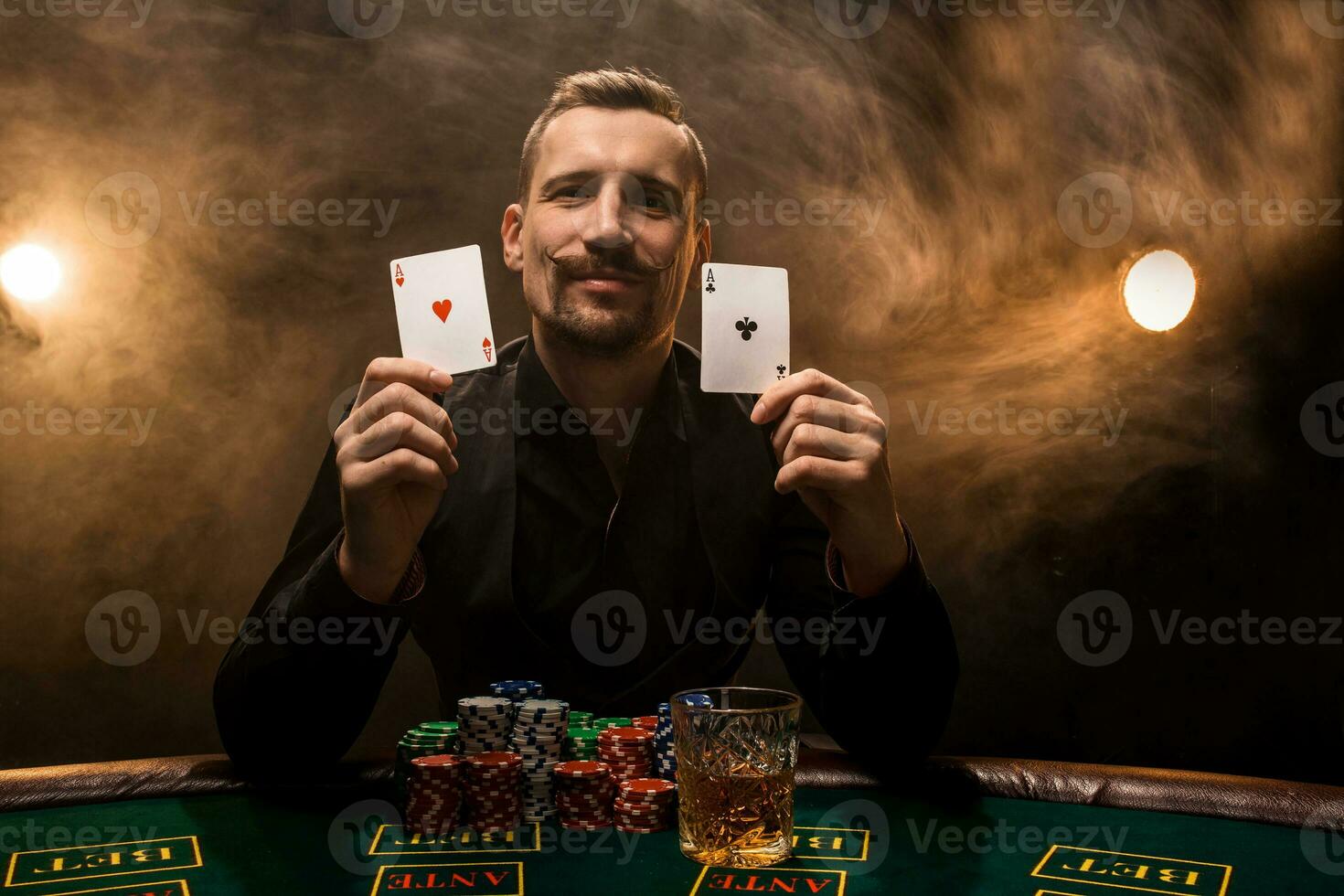 Mann ist spielen Poker mit ein Zigarre und ein Whiskey, ein Mann Show zwei Karten im das Hand, gewinnen alle das Chips auf das Tabelle mit dick Zigarette Rauch. foto