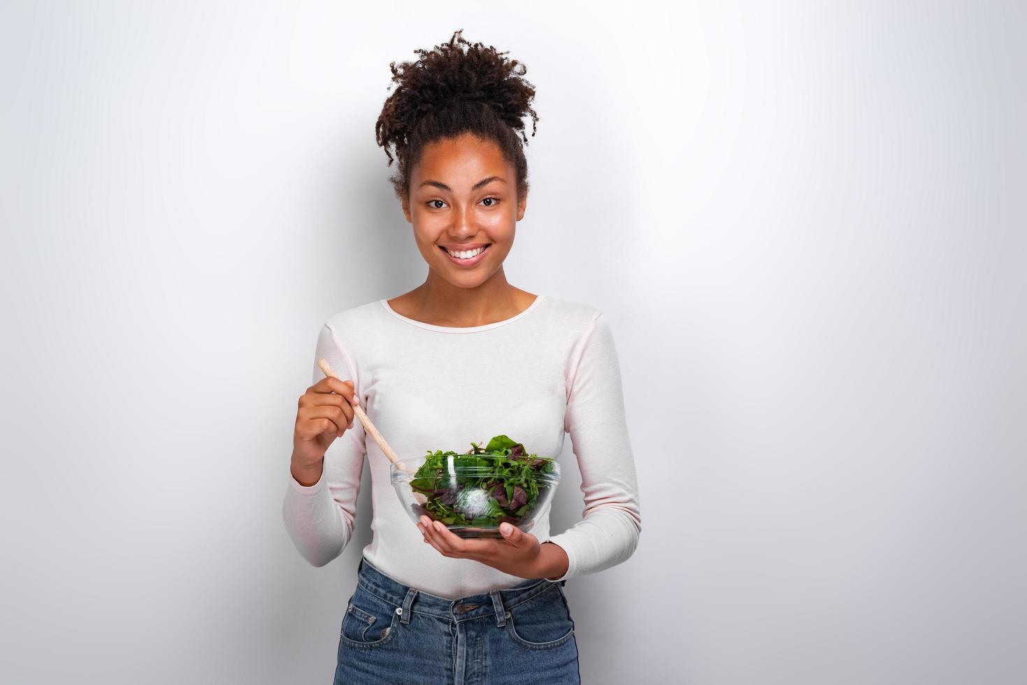glückliche Frau, die mit Salatschüssel über weißem Hintergrund steht foto