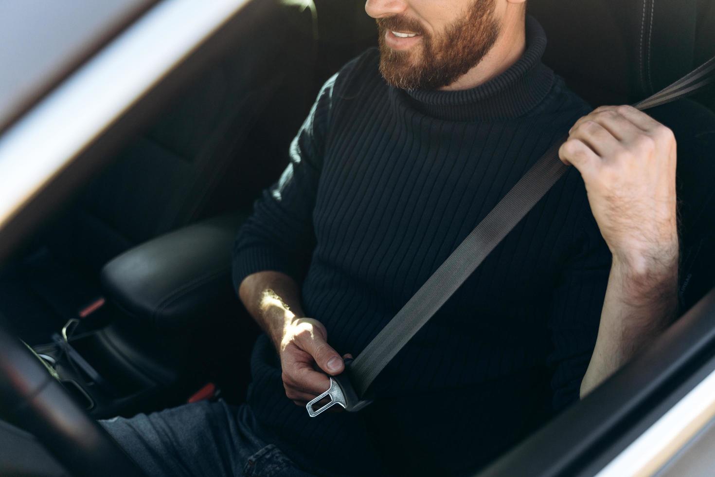 Nahaufnahme des kaukasischen jungen bärtigen Mannes in einem Auto, das seine Sicherheitsgurte vor dem Fahren anschnallt. selbstbewusster Kerl, der bei der Arbeit reitet. Stockfotos foto