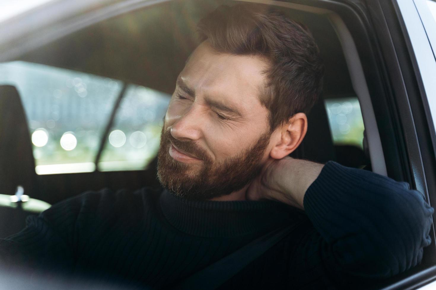 müder Geschäftsmann im Auto, der starke Nackenschmerzen und Nervenentzündungen nach langer Straße verspürt. Konzept für Transport- und Gesundheitsprobleme foto