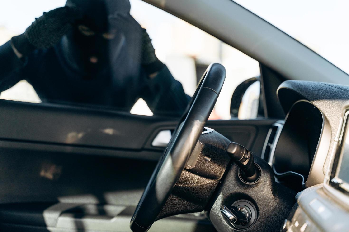 Blick aus dem Auto auf den schwarz gekleideten Mann mit Sturmhaube auf dem Kopf, der vor dem Diebstahl auf das Autoglas schaut. Autodieb, Autodiebstahlkonzept foto