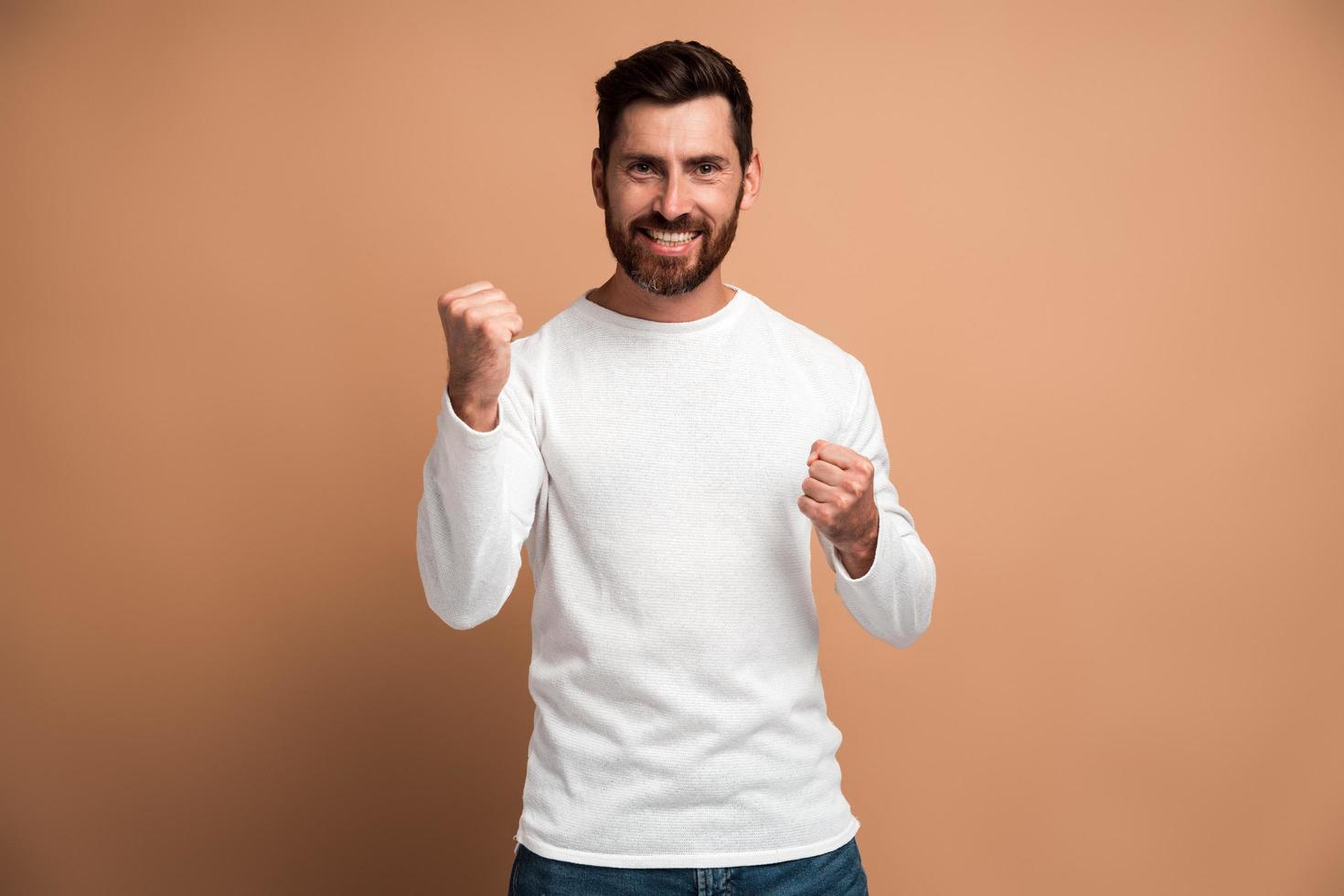 porträt eines ekstatischen brünetten mannes mit bart, der ja zeigt, dass ich es getan habe, geste und froh, kopierraum für werbung zu haben. Indoor-Studioaufnahme auf beigem Hintergrund isoliert foto