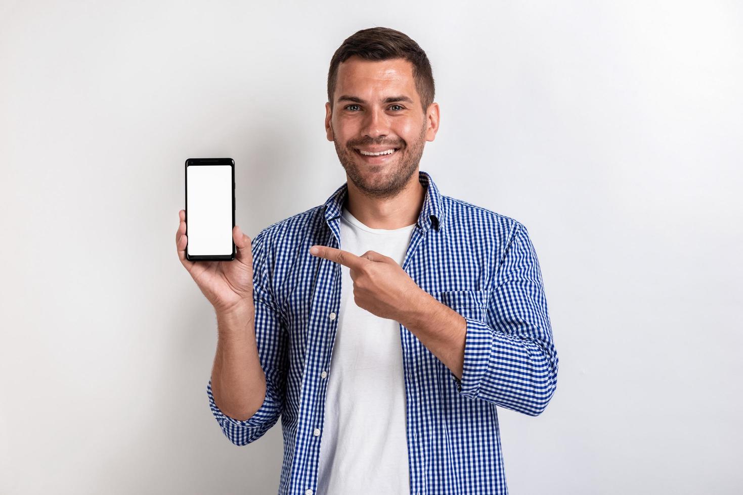 lächelnder Mann, der ein Smartphone hält und auf den Bildschirm zeigt - Modellbild eines weißen leeren leeren Bildschirms des Telefons foto