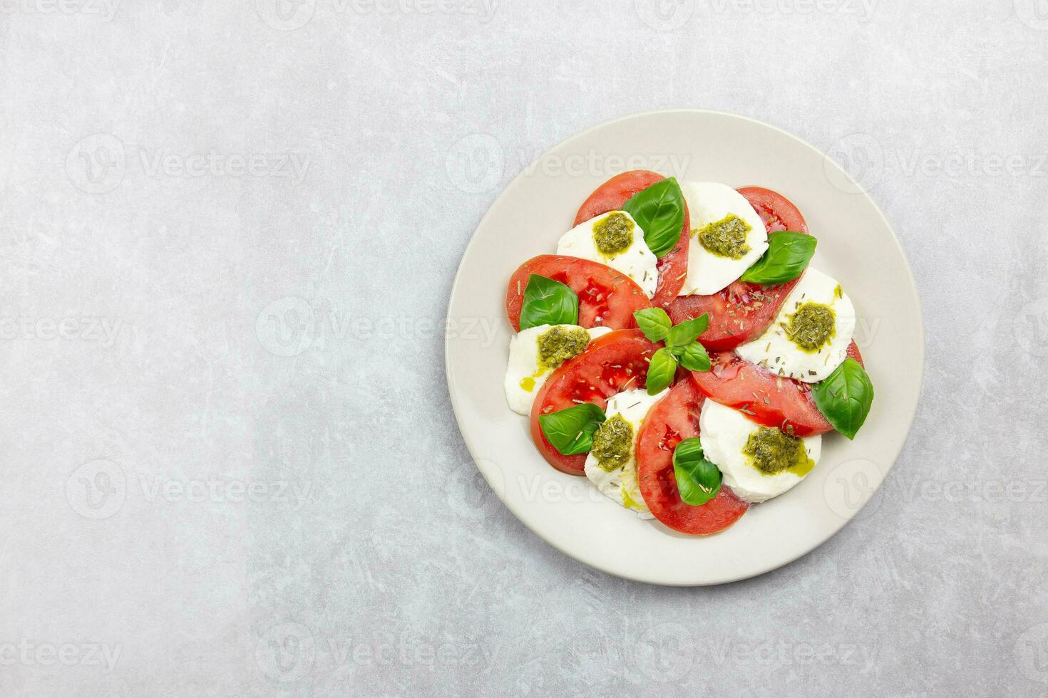 traditionell Italienisch Caprese Salat mit geschnitten Tomaten, Mozzarella, Basilikum, Pesto Soße und würzen auf ein Licht grau Beton Hintergrund. oben Sicht. Kopieren Raum. foto