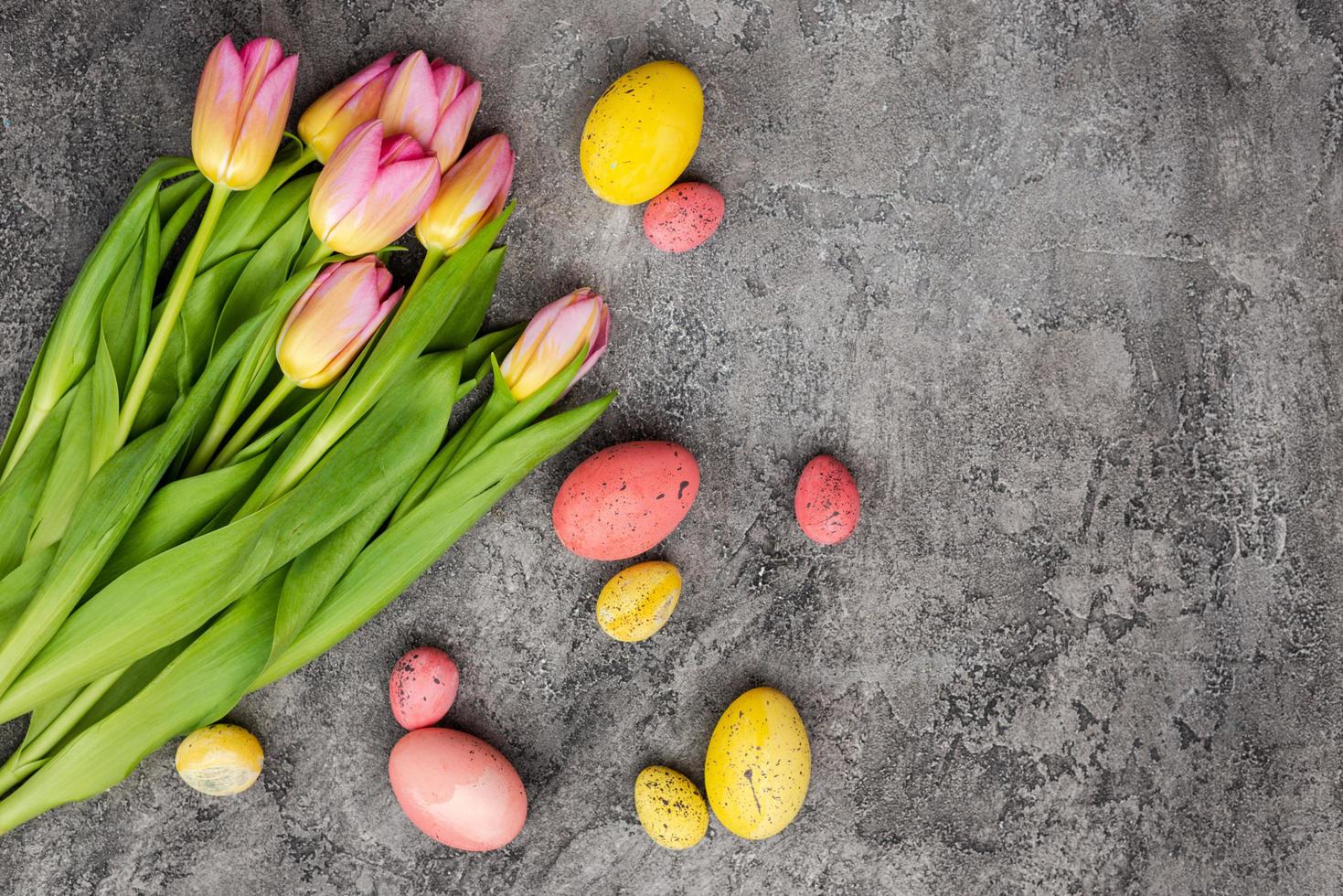 Strauß Tulpen und bunte Eier liegen in der Ecke auf grauem Putzhintergrund foto